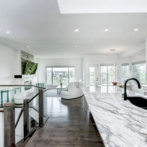 Arbour Lake, Calgary. Kitchen island in veined marble with a black undermount sink, open to the living room