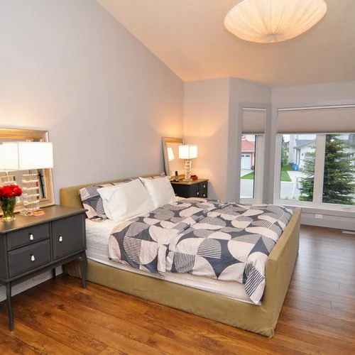 Chestermere, Alberta. Bedroom with a patterned duvet and a mirrored dresser beside the window