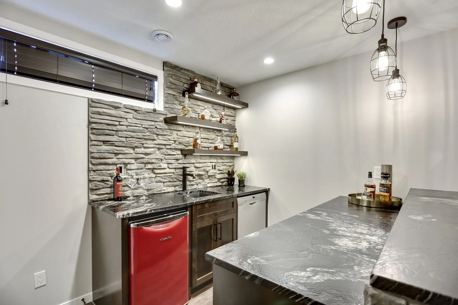 Basement bar with a stone wall and under counter fridge
