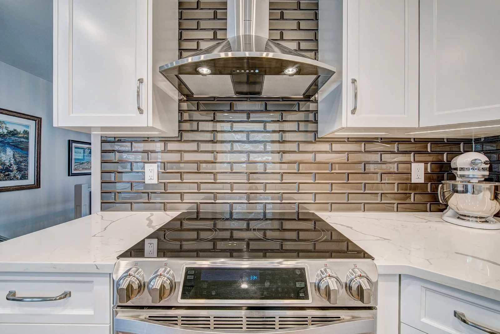 Slide in range under a stainless chimney hood against the bronze tile backsplash